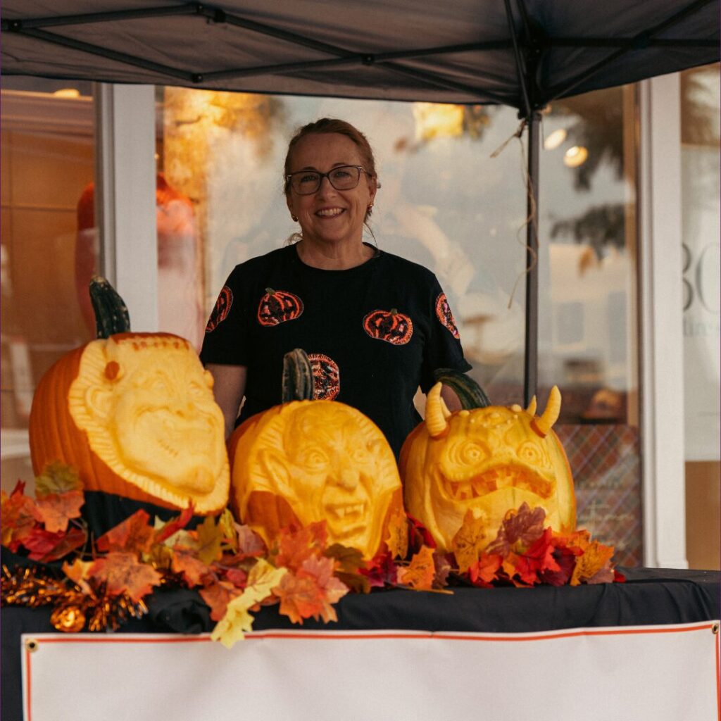 A smiling person standing behind three intricately carved pumpkins.